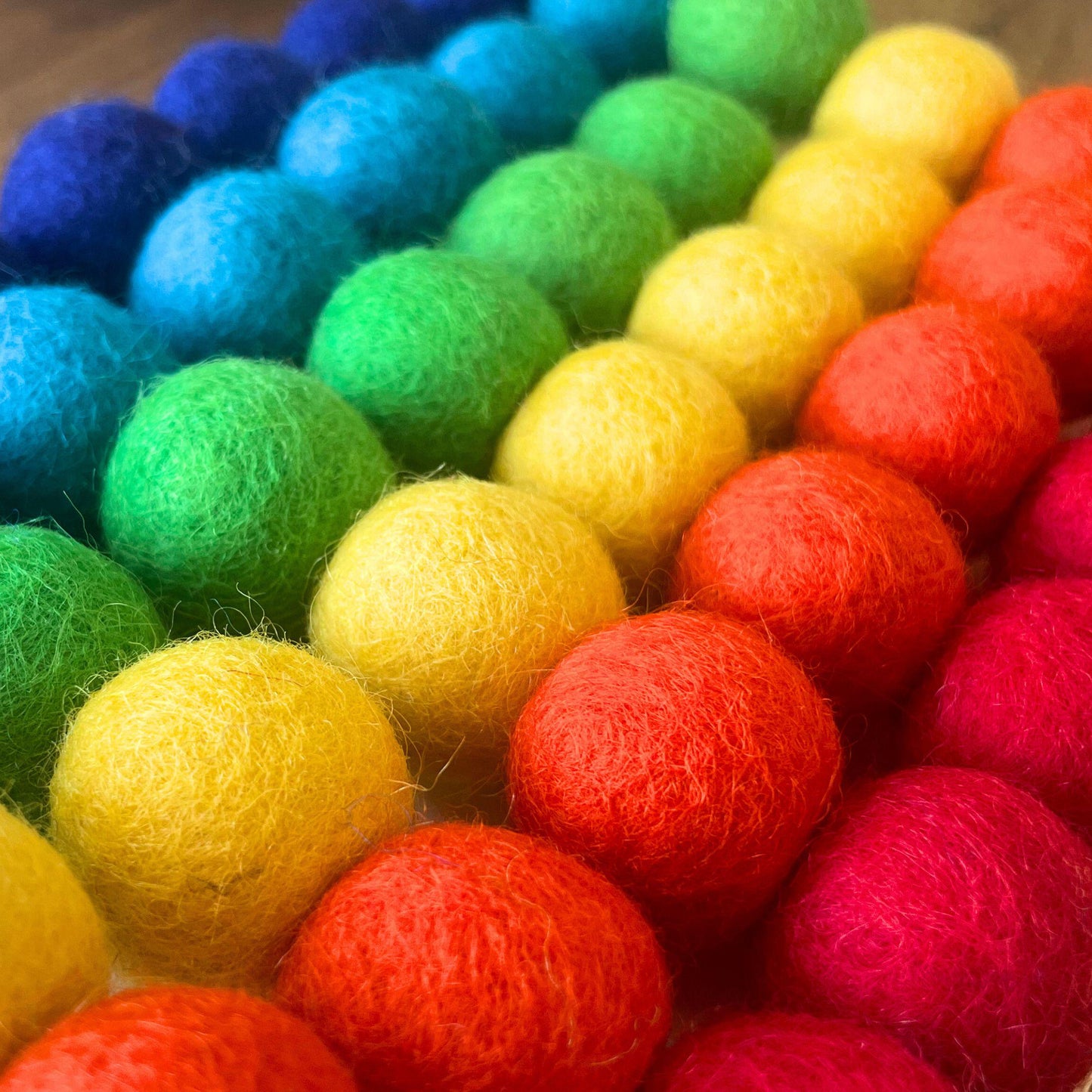A garland of multicolored felt balls arranged in a rainbow pattern, with colors including purple, blue, green, yellow, orange, and red.